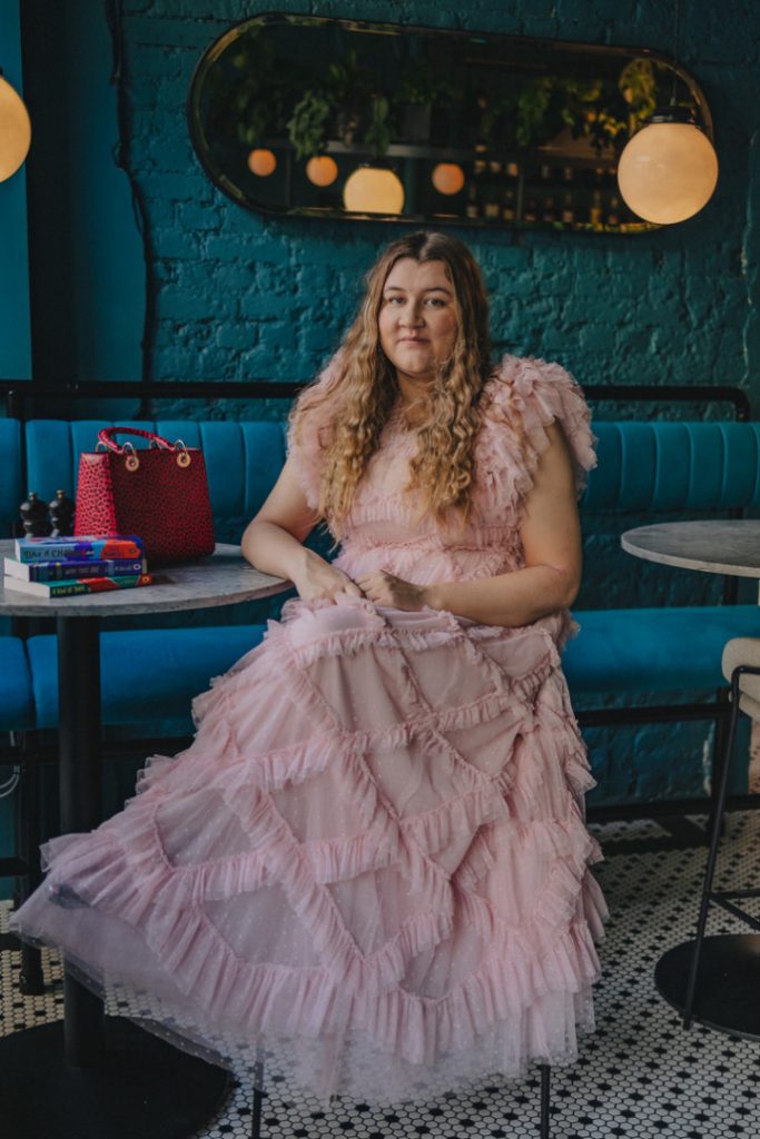 Elle McNicoll smiling while sitting in a pink ruffled dress.