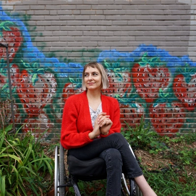 Rebekah Taussig sitting in her wheelchair in front of a wall with painted strawberries.