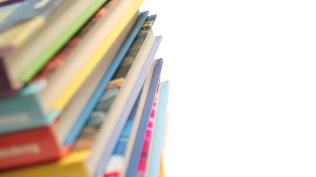 A colorful stack of hardcover picture books takes up half the photo. The white paper ends are facing the front of the photo, which is against a white background.