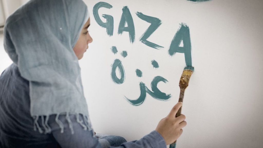 A woman writing "Gaza" in English and Arabic on a wall.