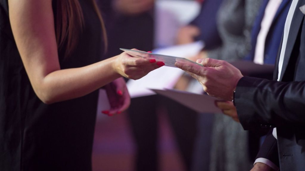 Two people exchanging a card at a ceremony.