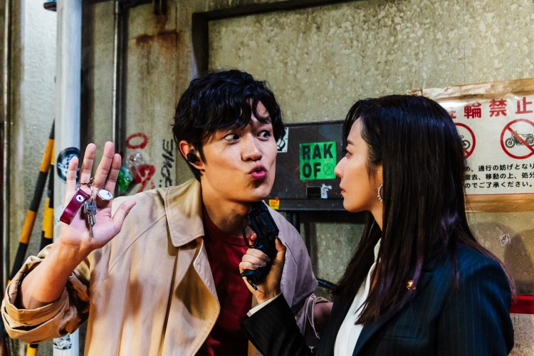Saeko Nogami holding a gun under Ryo Sabea's chin as he holds up a set of keys.