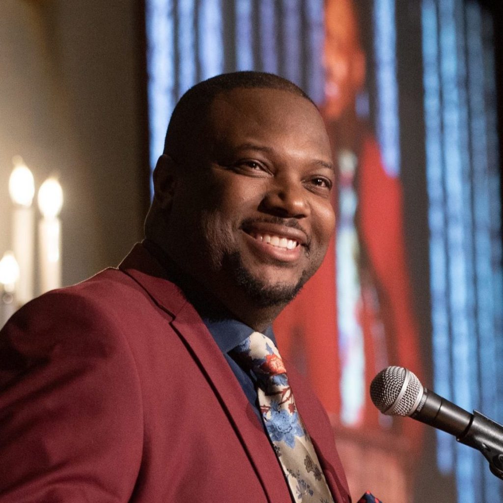 Author Dr. George James smiling and standing behind a podium with a microphone.