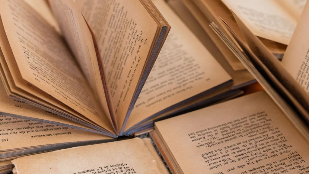 Open books cover a table. Some books have pages sticking straight up.
