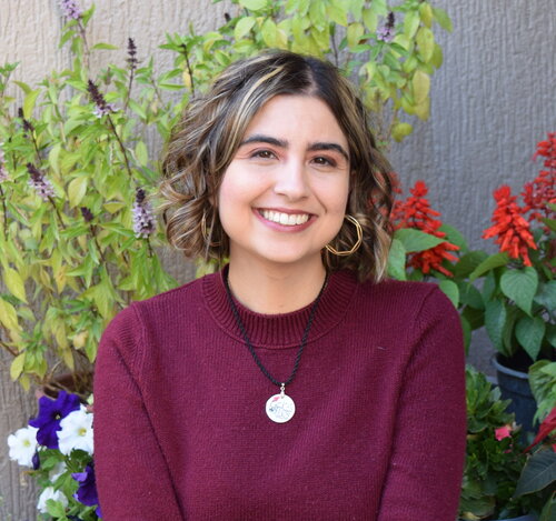 Chelsea Abdullah smiling widely and surrounded by pretty flowers.