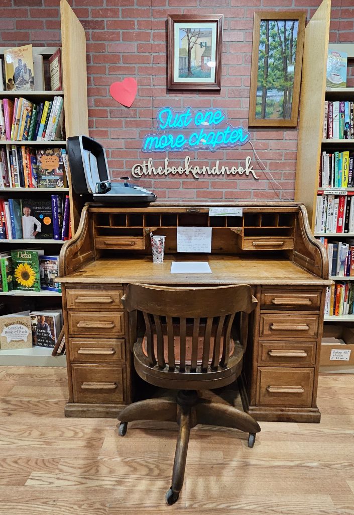 Rolltop desk at the Book and Nook with a neon sign that says Just one more chapter.