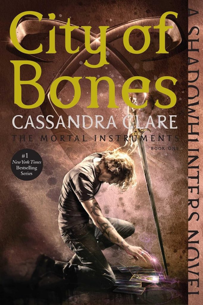 City of Bones by Cassandra Clare. The cover of a blonde boy with Shadowhunter tattoos, a sword, touching the Mortal Cup in a tarot card.