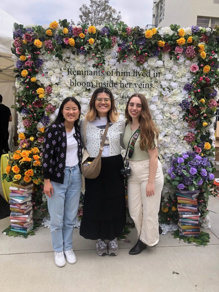 Article writer with friends in front of one of the photo-op backgrounds filled with flowers and piles of books.