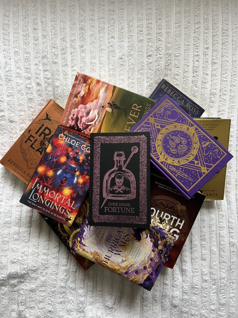 On a white fabric, numerous fantasy books are stacked in a way that makes a circle.