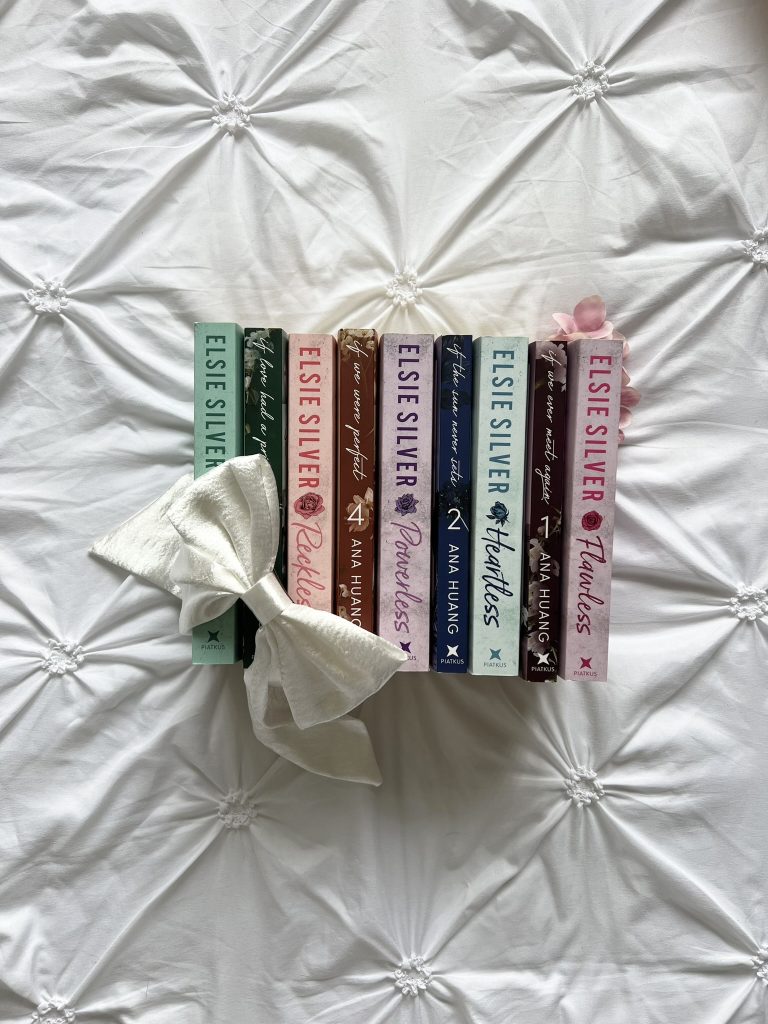 Books by Elsie Silver and Ana Huang are stacked spine up on a white fabric. On top of them is a white bow.