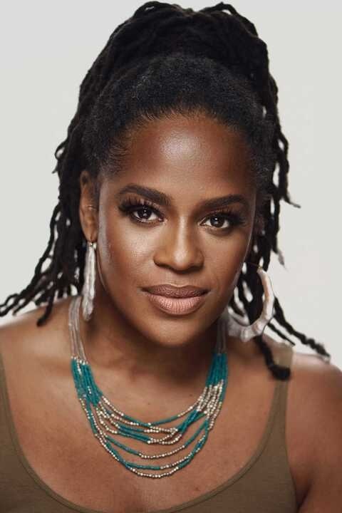 Headshot of Thembisa S. Mshaka. She is against a white wall wearing blue and gold beaded necklaces.