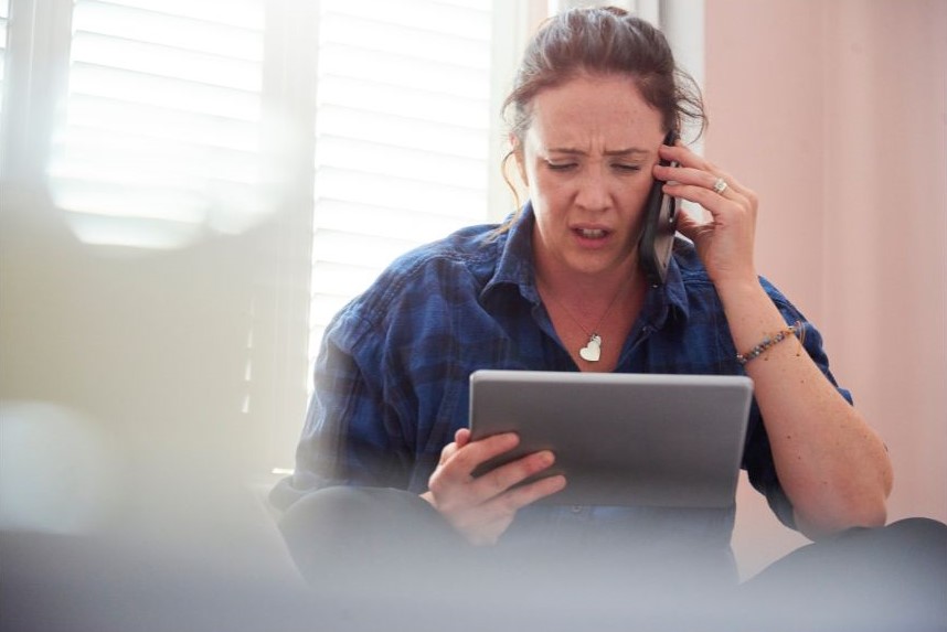 A woman staring confused at her tablet while on the phone.