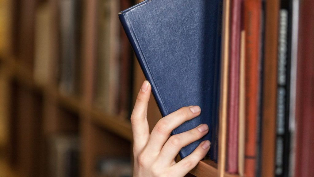 Hand pulling a blue book from a bookshelf.