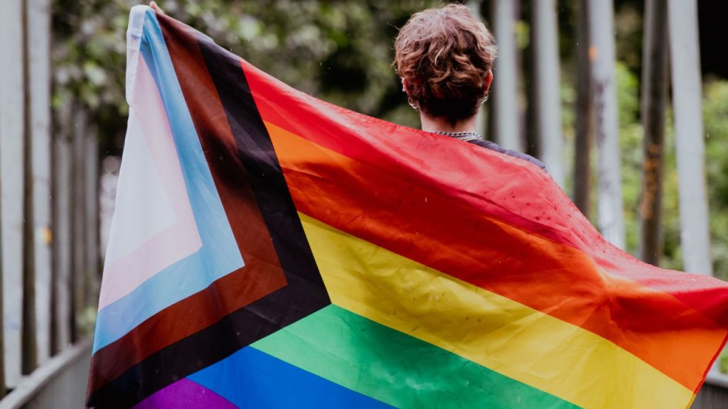 A person holding an LGBTQ+ flag behind their back.