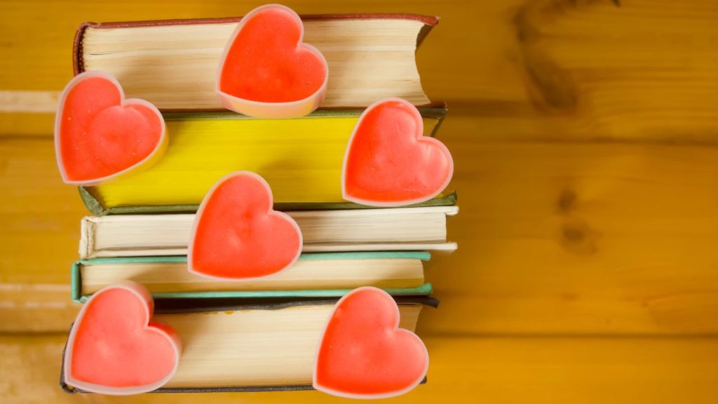 A stack of various books with six red hearts placed on top of the books.