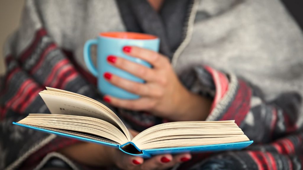 person holding a mug in one hand and a book in the other