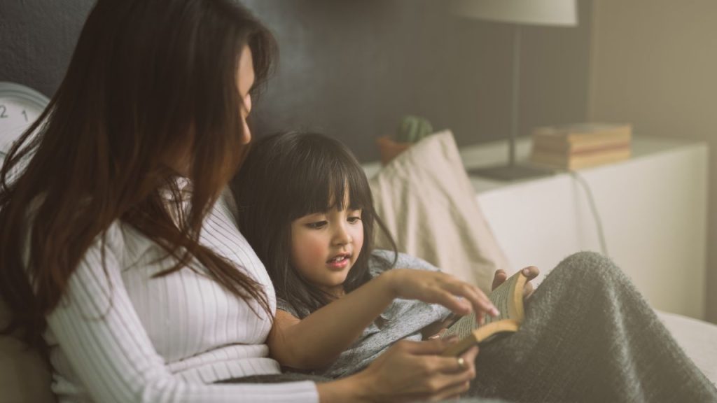 Mother and daughter cuddling while reading a book