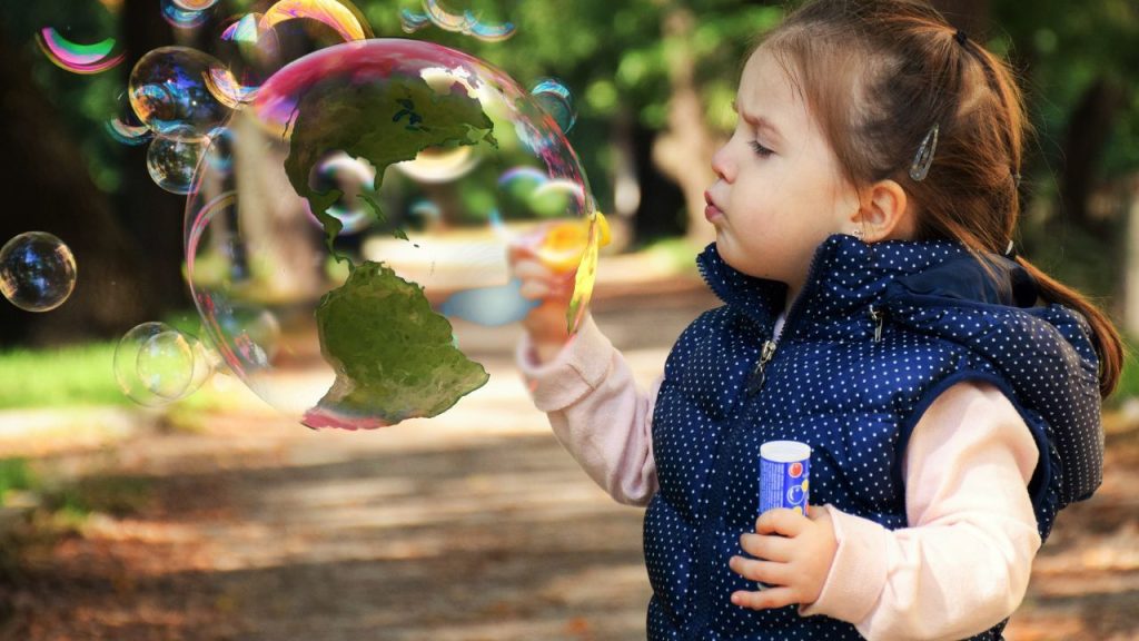 A little girl blowing bubbles, on huge bubble takes the image of the earth.