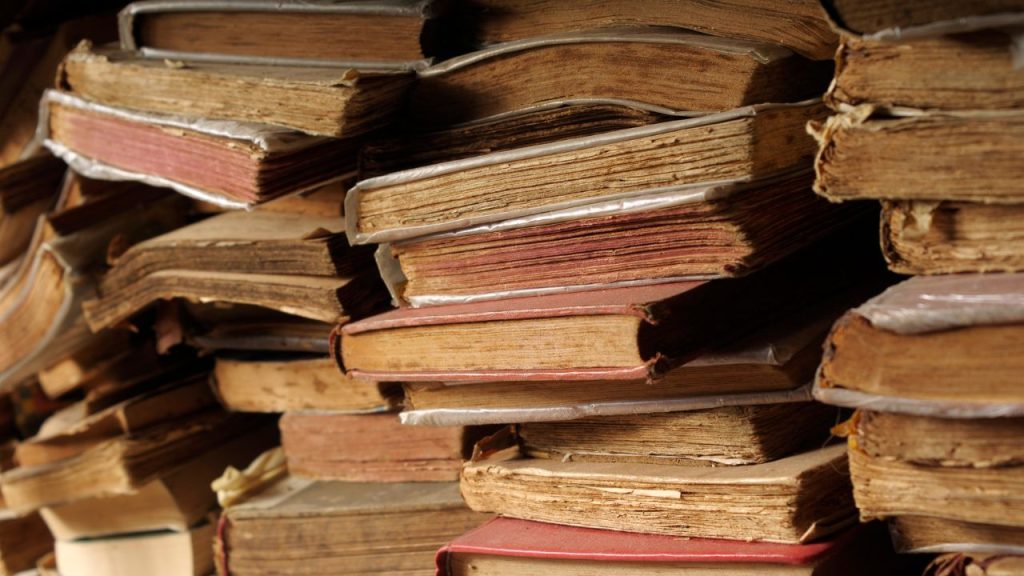 Stacks of worn, yellowing, antique books with red and gray covers.