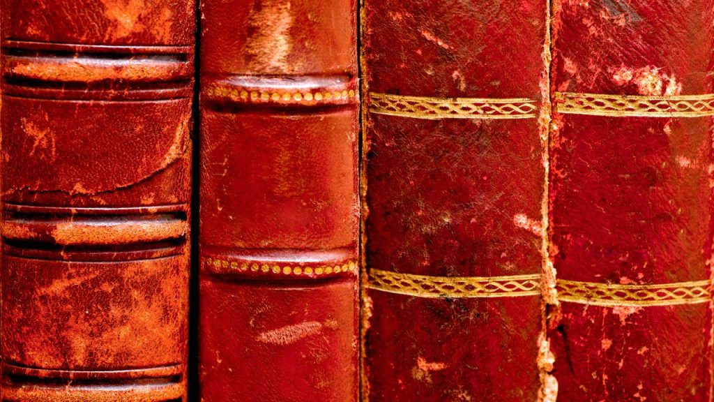 Four spines of worn-in, bright red antique books with dainty gold stripes.
