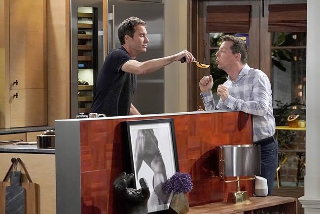 A man holding a spoon out to another man to taste test the food he's cooking.