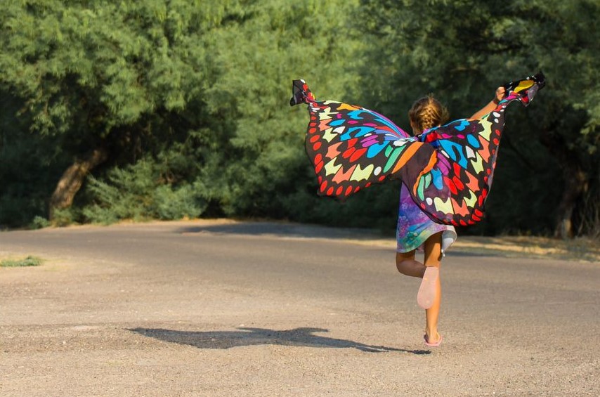 A young child holding fabric behind them as it billows as they run.