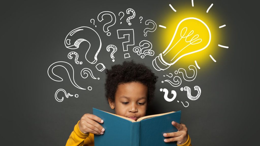 A child reading a book, with many question marks with a light bulb above him to signify how he's thinking and learning.