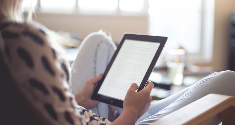 Person sitting cross-legged reading on a tablet.