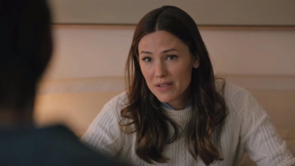 A woman with long brown hair, wearing a white sweater, looks concerned as she talks to someone off-camera. The setting appears to be a cozy, intimate room, suggesting a serious or heartfelt conversation.