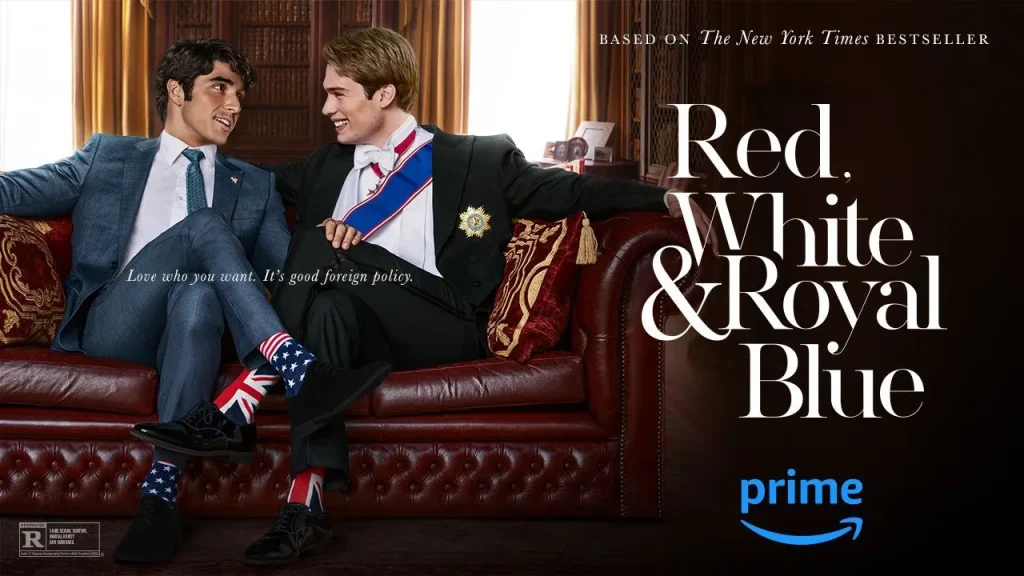 Two young men are sitting on a luxurious red leather couch. One wears a dark suit and blue tie, sporting socks with the British flag, while the other is dressed in a royal uniform with a sash, smiling at each other. The poster text reads, "Red, White & Royal Blue" and "Love who you want. It's good foreign policy." The Prime Video logo is at the bottom right.