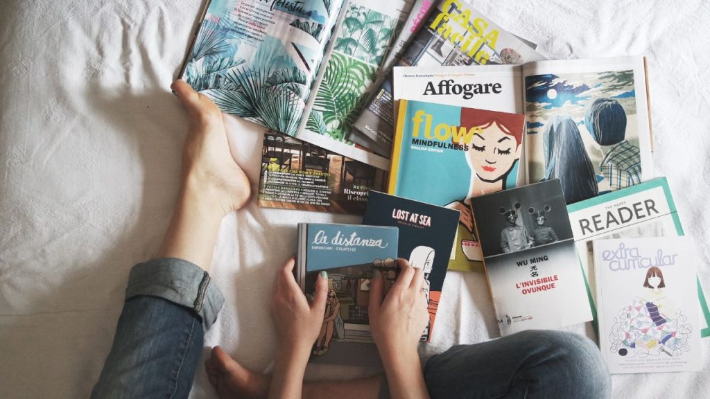 Woman sitting on a bed with books and magazines spread out before her.