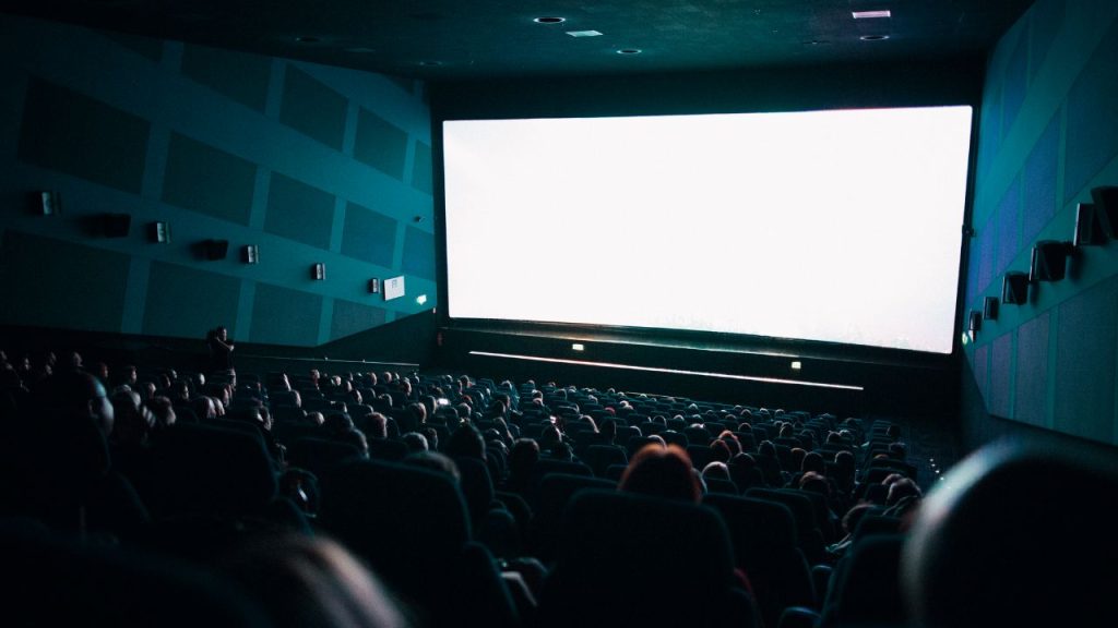 An elevated view of a crowd watching a white screen in a movie theater.