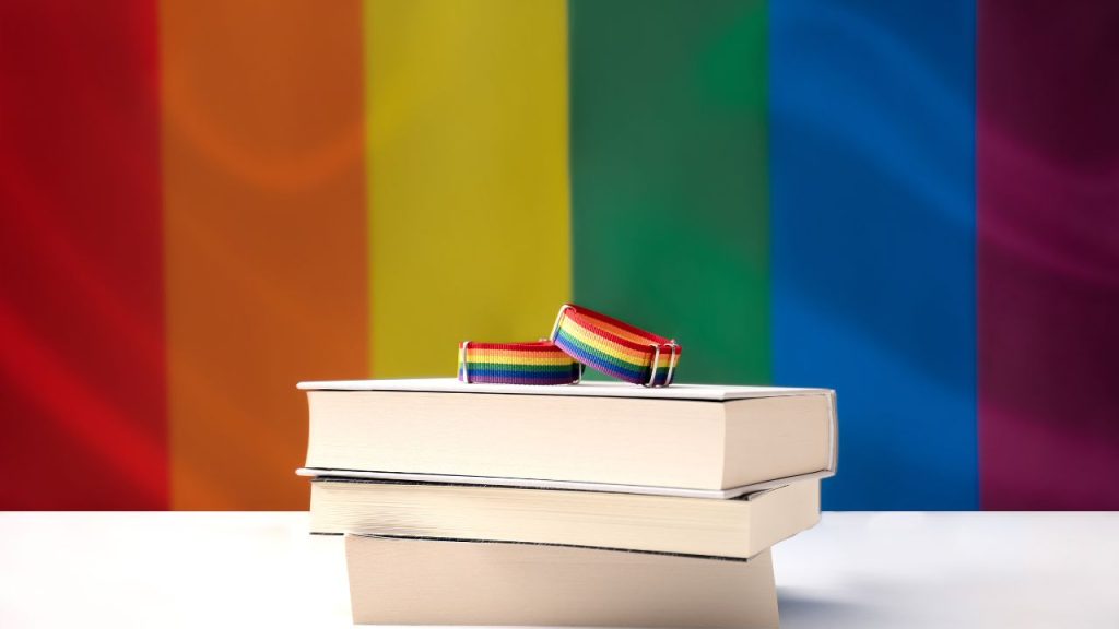 stack of bookks with a pride flag in the background