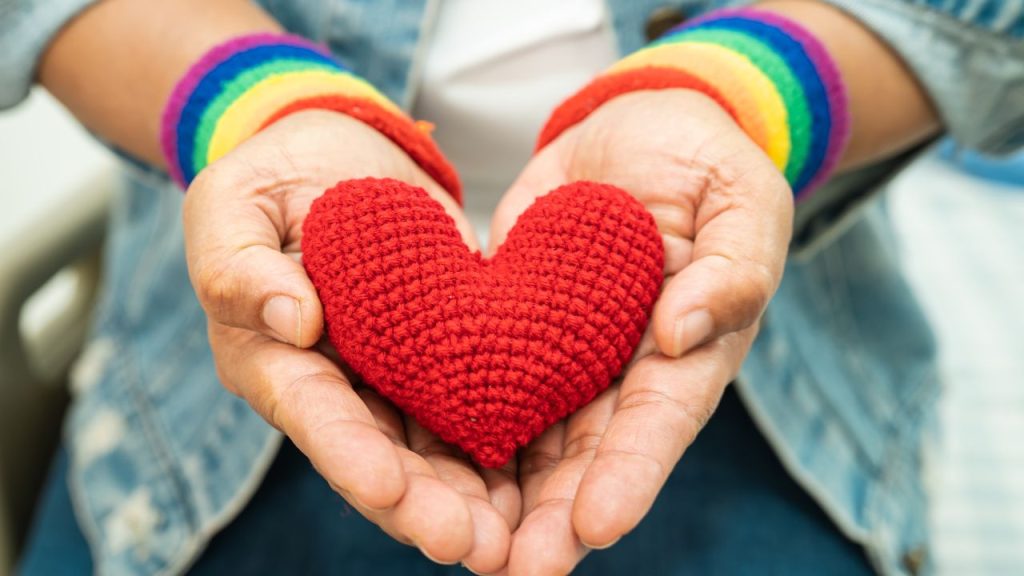 two hands with pride wrist bands holding a heart