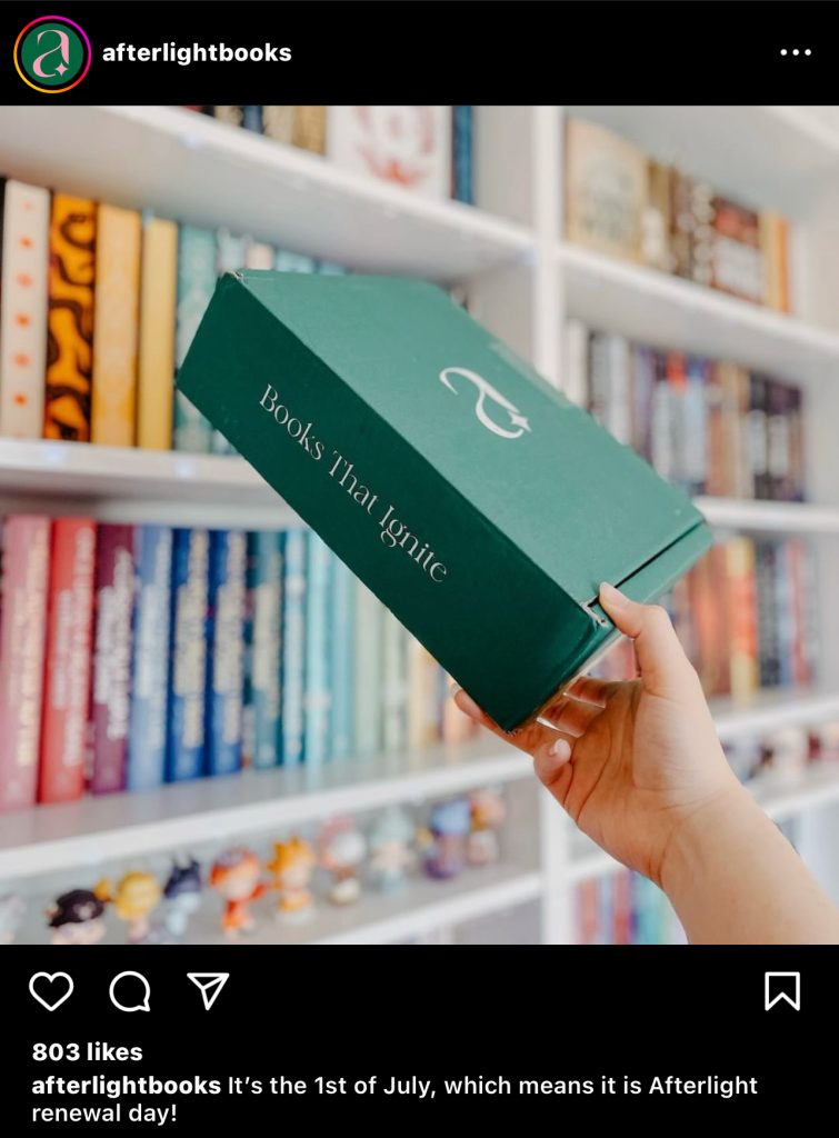 Instagram post by Afterlight Books of a person holding a green box in front of a colorful bookshelf.