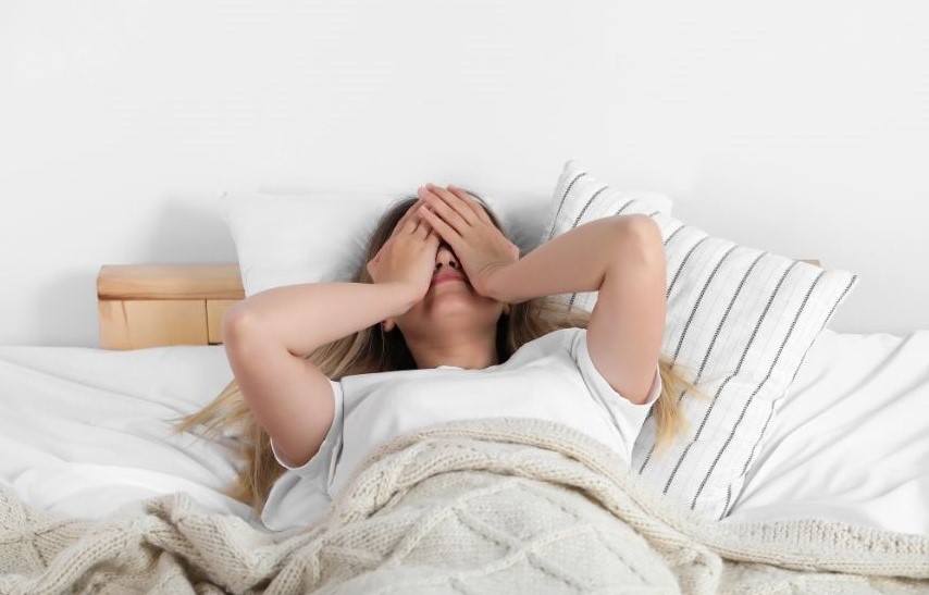 A woman lying in bed with her hands covering her face.