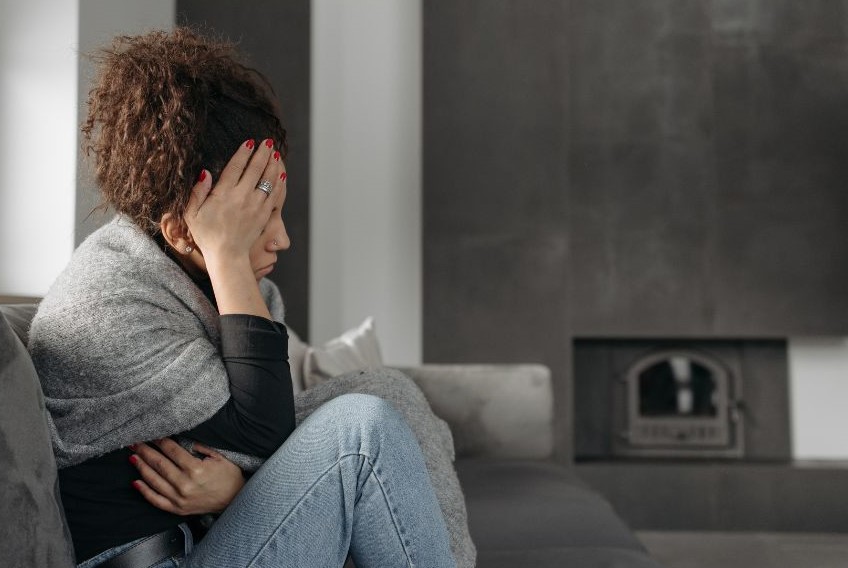 A woman sitting on a couch witha hand on her forehead.