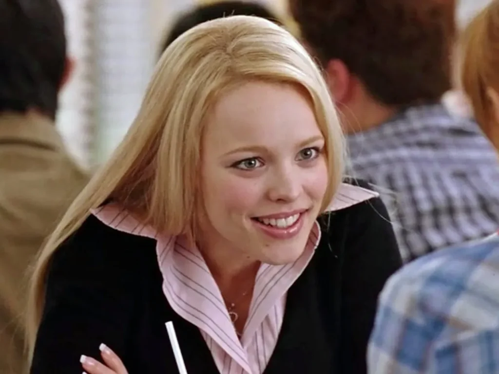 Regina George leaning over the table with a smile.