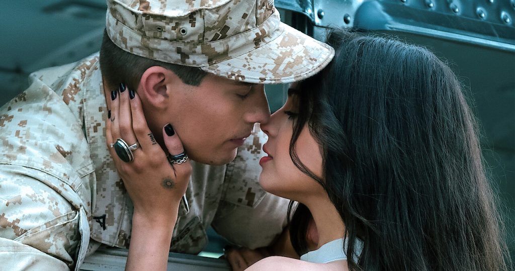 Movie still from Netflix's "Purple Hearts" with Sofia Carson and Nicholas Galitzine kissing when he leaves for deployment.