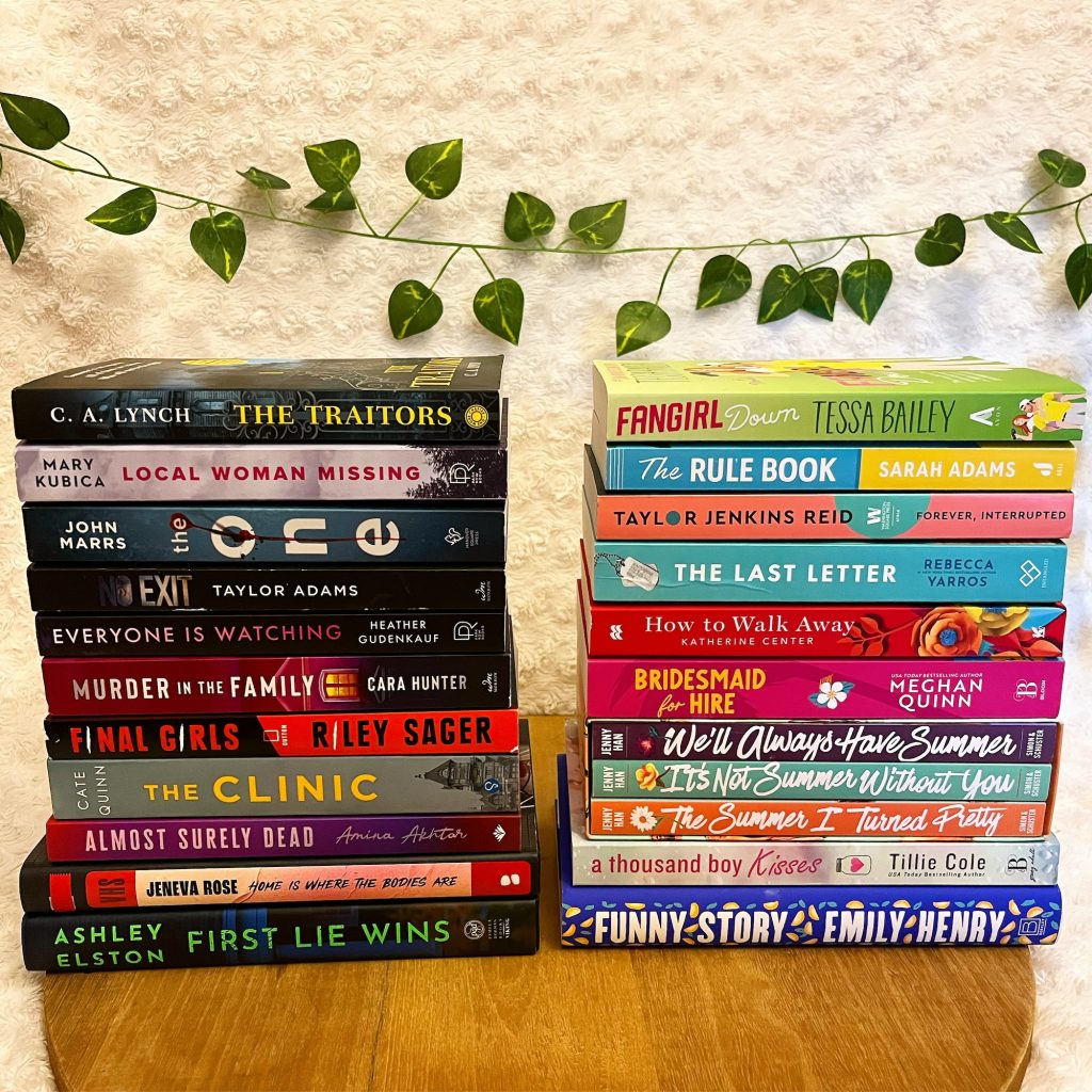Two stacks of books sitting in front of a fuzzy white blanket and a vine of green leaves.