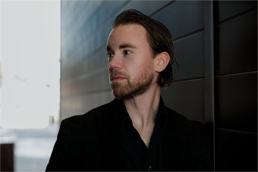 Adam Prottle, while man with a beard standing before a black building