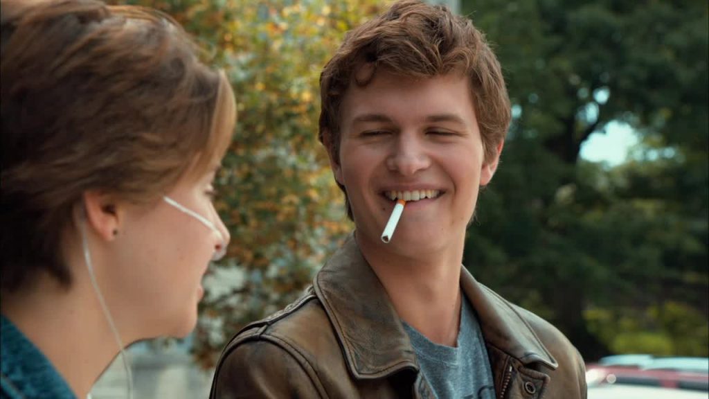 Augustus Waters, portrayed in a scene from 'The Fault in Our Stars,' sitting across Hazel with a cigarette in his mouth, symbolizing defiance against his cancer."