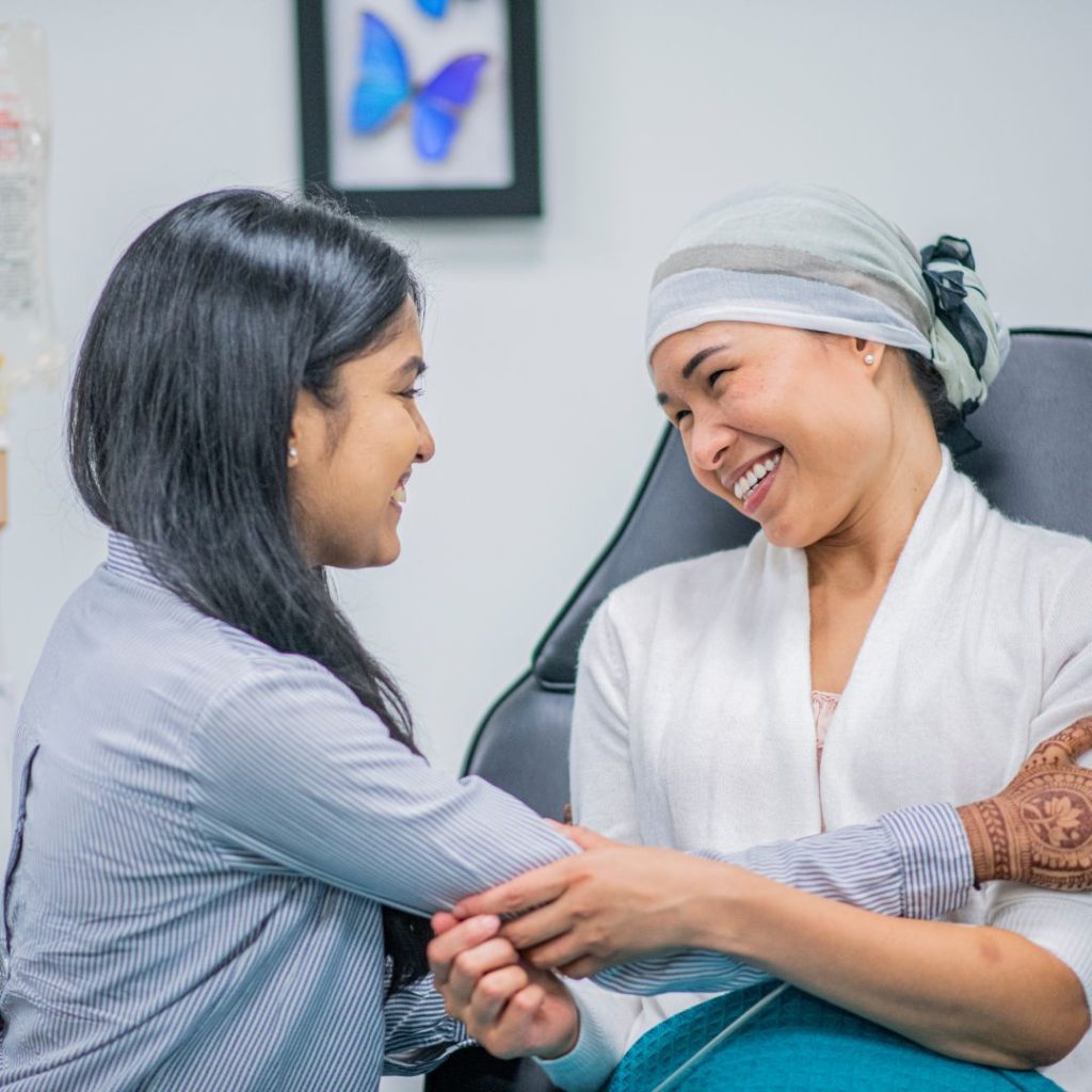 Two women smiling at each other warmly, preparing to embrace. One woman, a cancer patient, looks joyful, while the other, likely a visitor, exudes happiness.