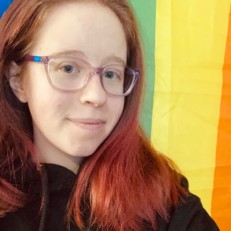 Haley smiling in front of a rainbow pride flag.