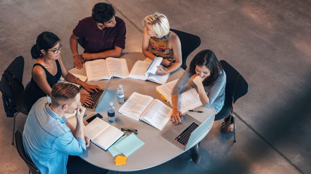 A group of people sitting at a table surrounded by books and laptops.