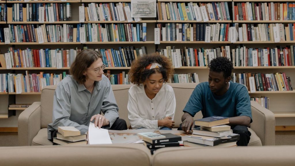 Three people studying and sitting on a couch in a library.