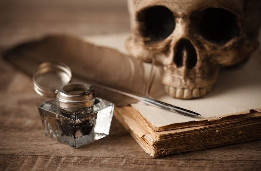 A skull sitting on top of papers with a pen and ink well sitting next to them