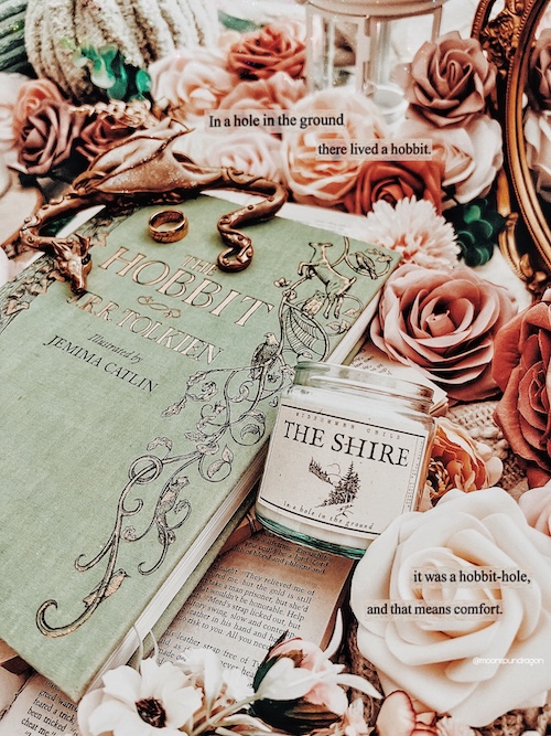 Book cover of "The Hobbit" by J.R.R. Tolkien, surrounded by flowers and a "The Shire" candle.