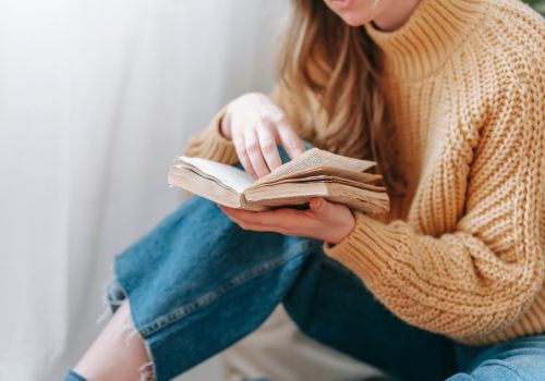 A woman in a beige sweater reading a book.