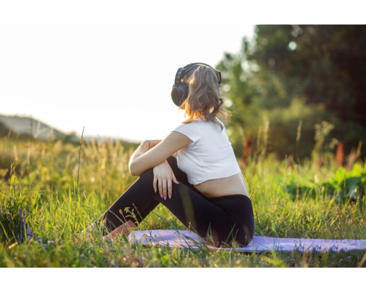 A woman listening to an audiobook outside on a yoga mat while admiring the beauty of nature.